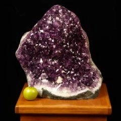 Large purple amethyst geode with a small green apple on a table