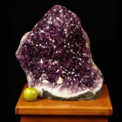 Large purple amethyst geode with a small green apple on a table